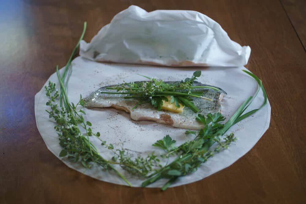 An assortment of fresh herbs, seasoned trout, and a fish packet ready to bake.