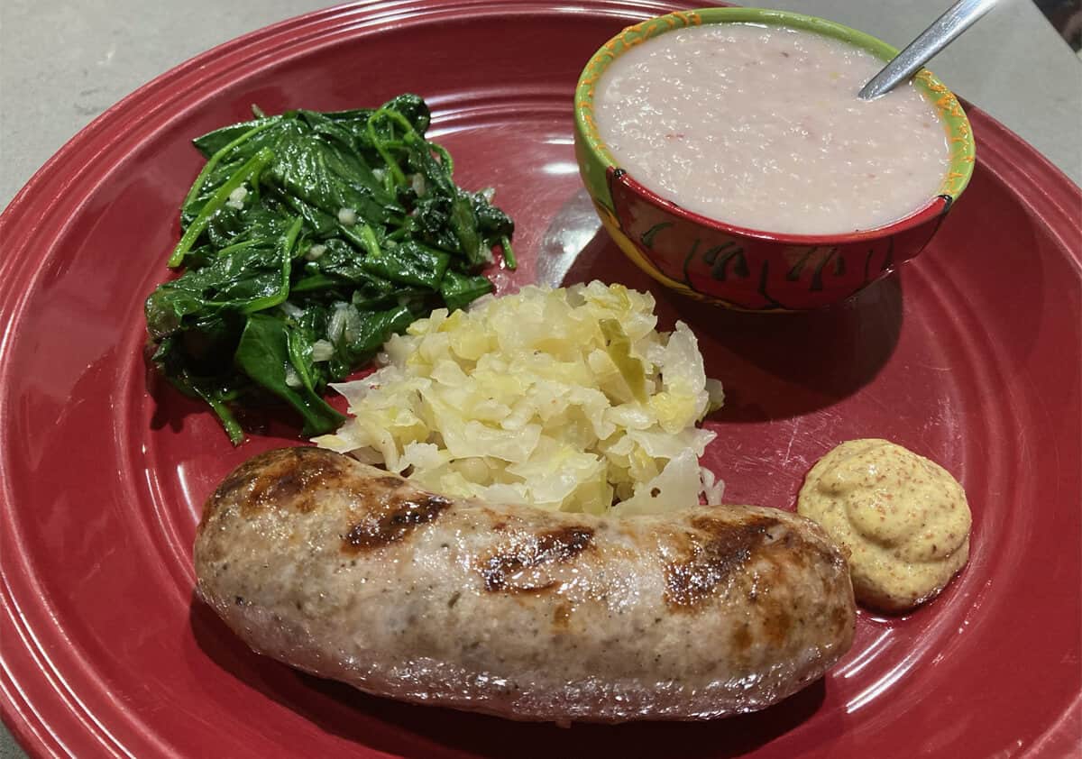 brats, grits, and greens served on a red plate